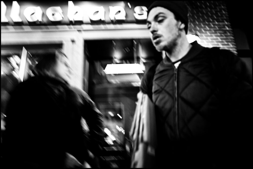 Black and white photograph of a man walking in front of a building.