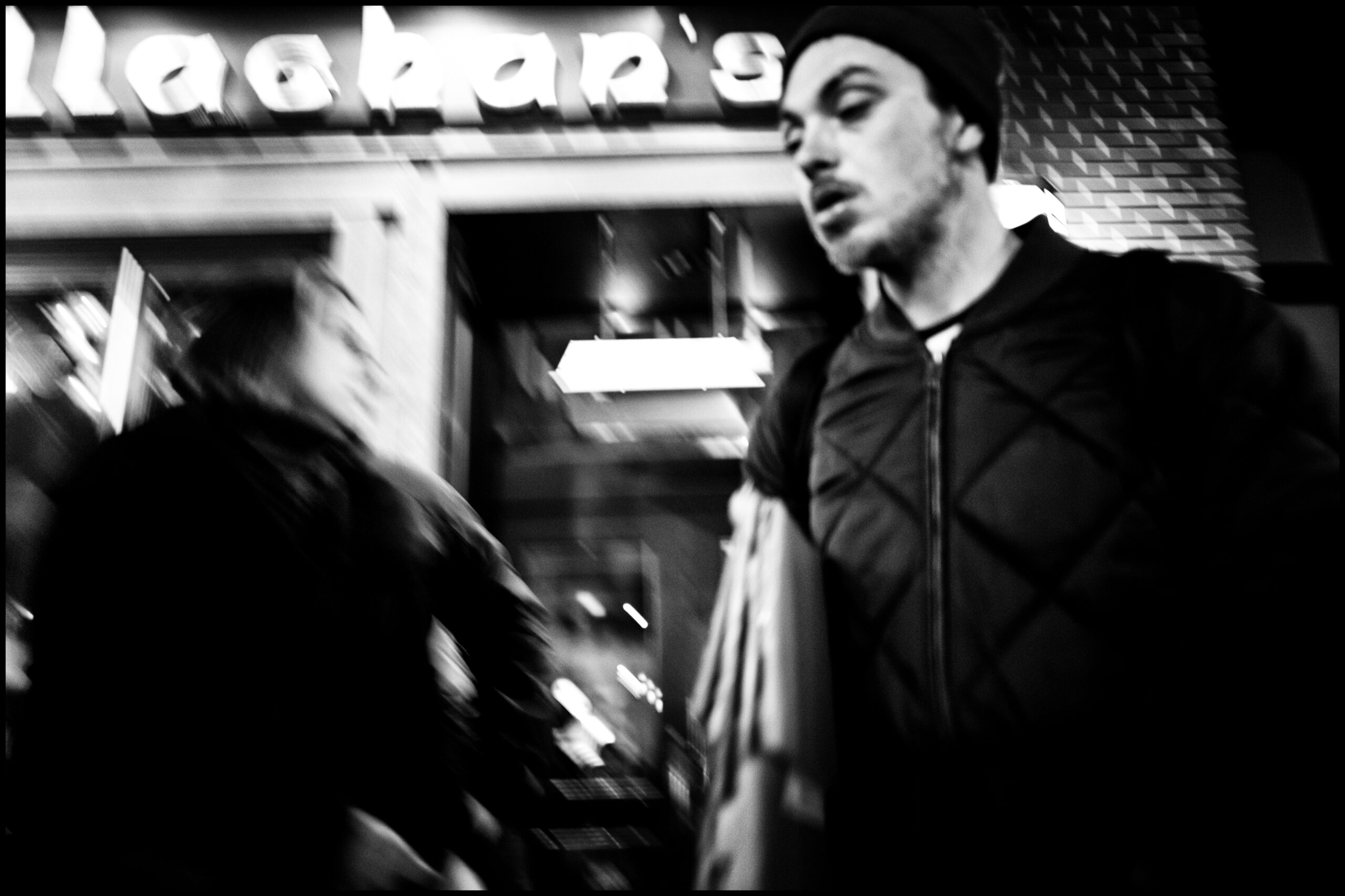 Black and white photograph of a man walking in front of a building.