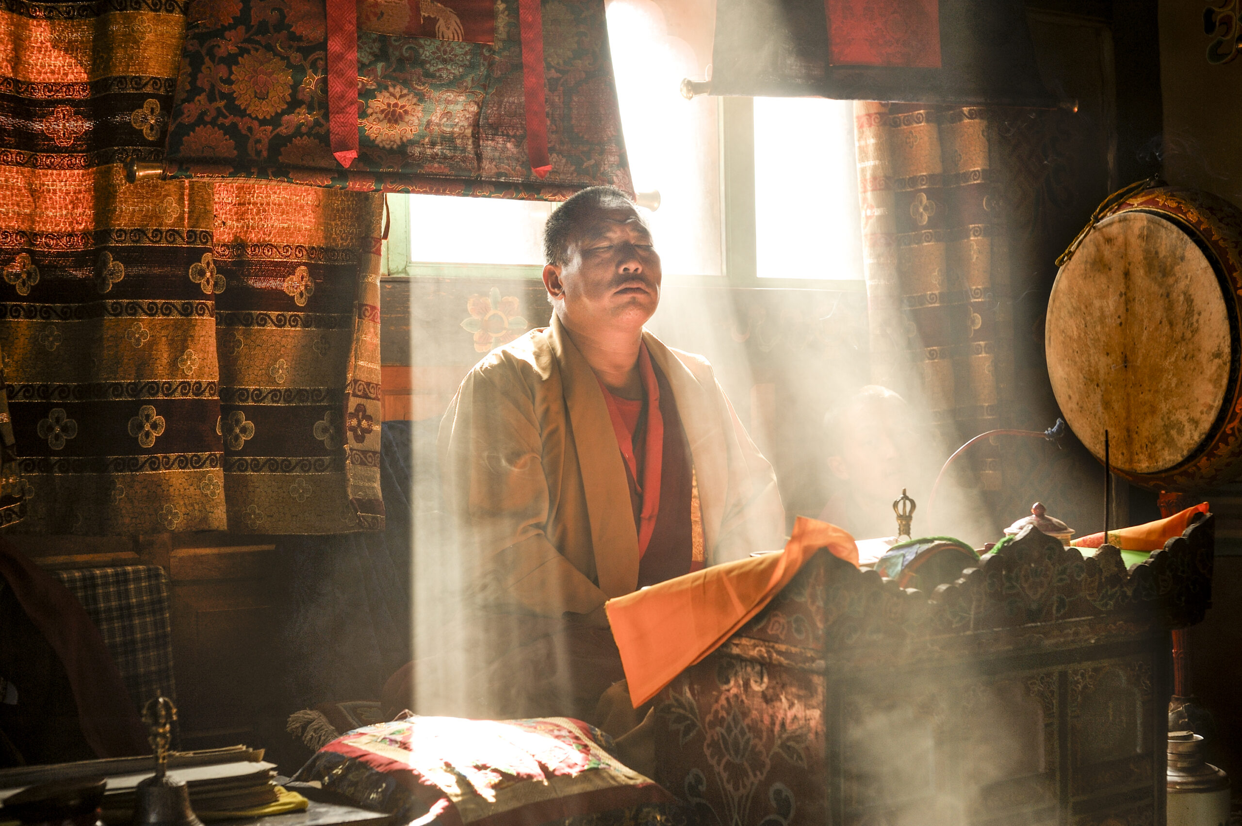 Monk sitting near a window with rays of light shining on his back.
